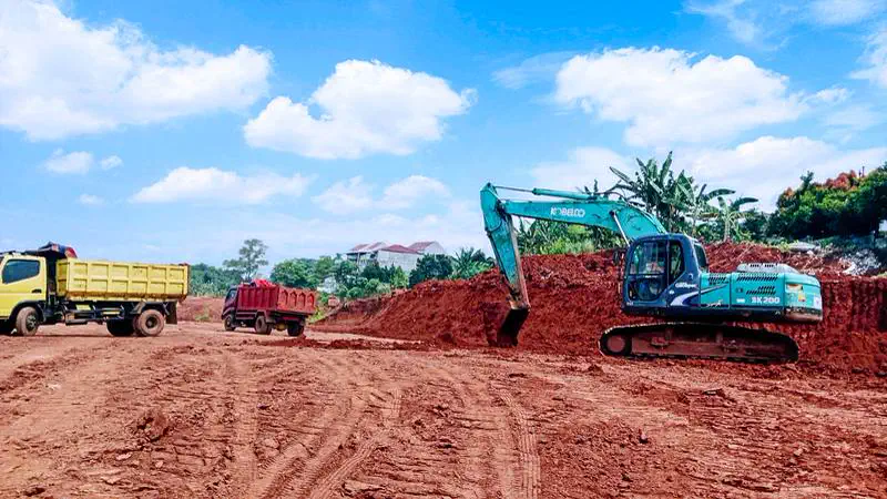 Excavator Kobelco memuat dump truck pada proyek pematangan lahan